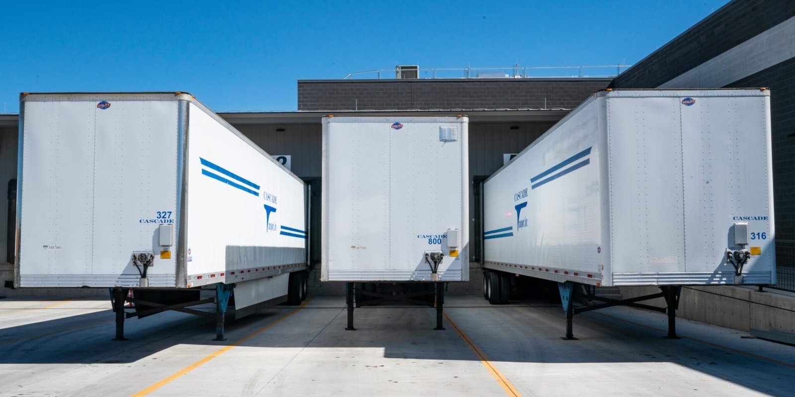 Three white cargo trailers parked at an industrial shipping dock under clear blue skies.